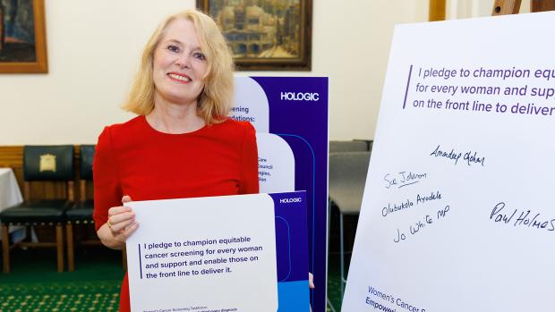 Blonde women in red dress holding pledge board at event